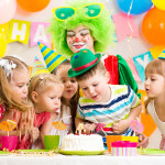 Children With Clown Celebrating Birthday Party And Blowing Candl